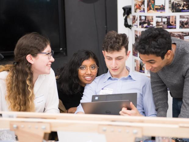 male and female students huddled around laptop smiling